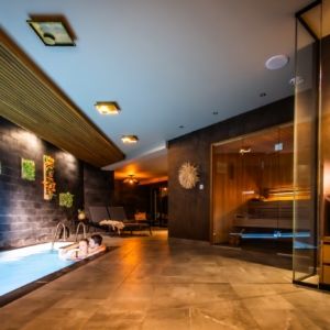 Couple se relaxant dans une piscine intérieure éclairée, avec un sauna vitré et une décoration élégante
