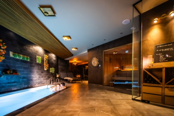 Couple se relaxant dans une piscine intérieure éclairée, avec un sauna vitré et une décoration élégante