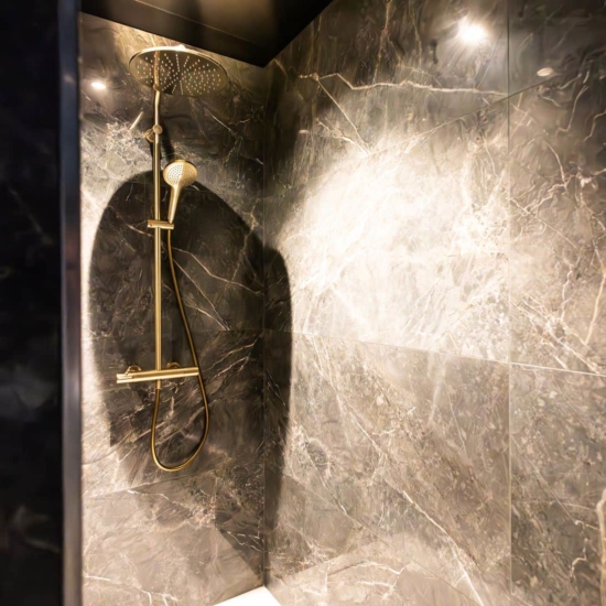 Douche italienne avec revêtement en marbre sombre et pommeau doré dans une suite haut de gamme